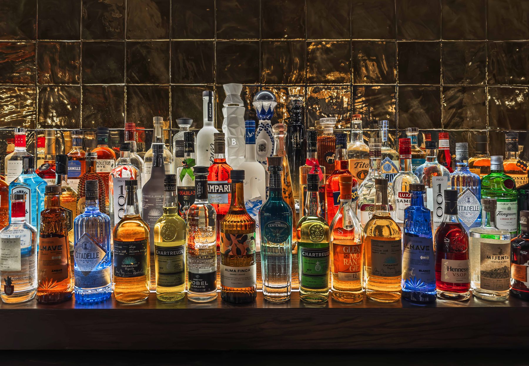 The backbar, lit bottles against gold tile in the 65-seat lounge below East 17th Street